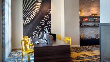 A modern hotel room with a dark wood desk, yellow chairs, a large wall mural, and a patterned carpet.
