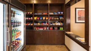 A hotel pantry with a refrigerator stocked with beverages and shelves with snacks and condiments. - TownePlace Suites by Marriott Seguin (Seguin)