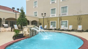 A swimming pool with a water feature, lounge chairs, and a stone wall. - TownePlace Suites by Marriott Seguin (Seguin)