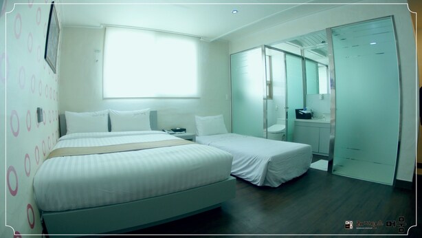 A hotel room with a large bed, a smaller bed, a desk, a chair, a wardrobe, and a bathroom. - Residence Mumum Hotel (Busan)