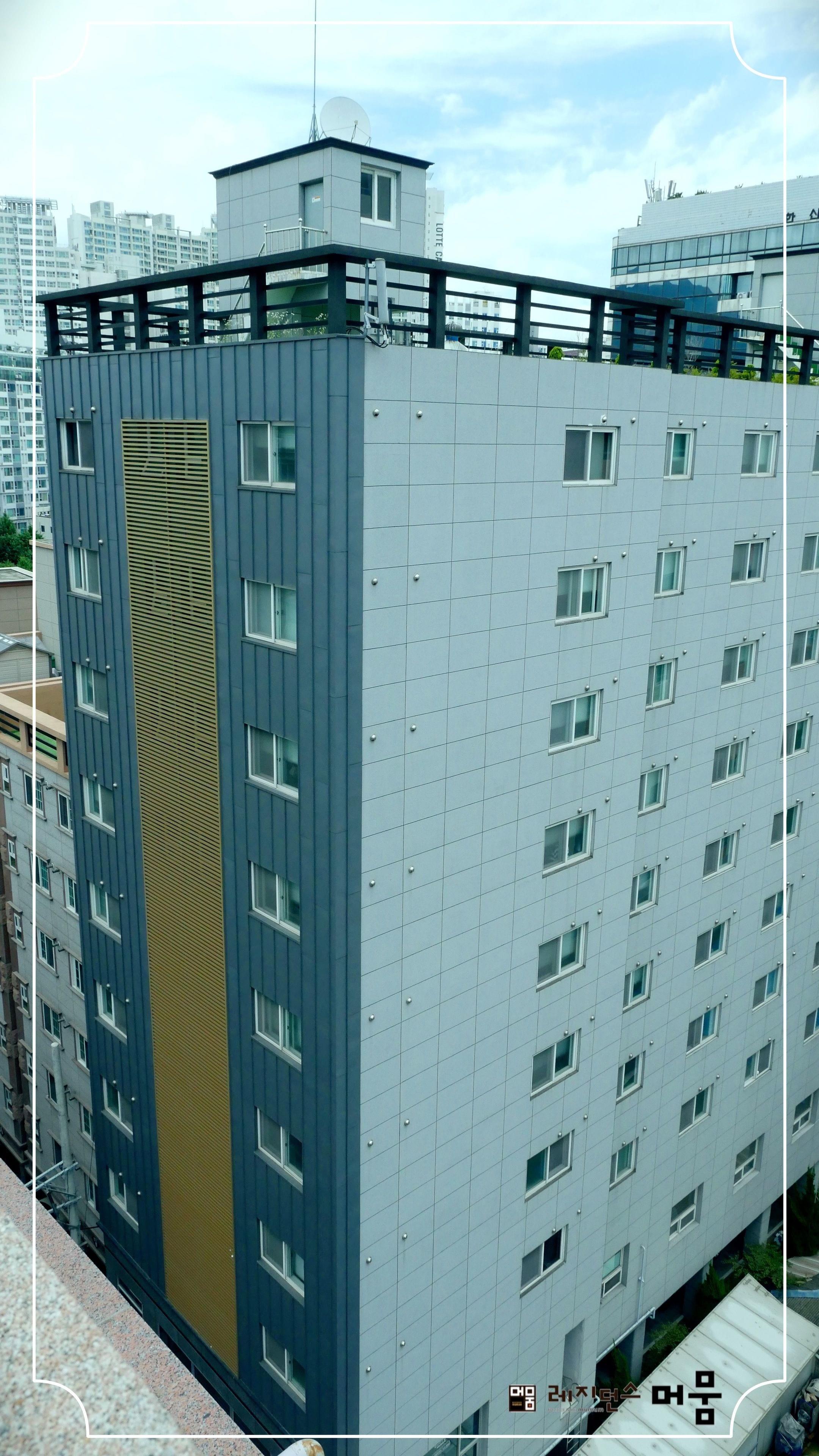 A modern high-rise building with a distinctive facade, featuring a combination of grey and blue panels, and a prominent vertical section with a textured pattern.