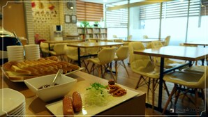 A dining area with tables and chairs, a buffet with bread and a bowl of food, and a brick wall with framed pictures. - Residence Mumum Hotel (Busan)