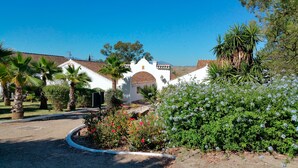 Un bâtiment blanc surmonté d’un toit recouvert de tuiles rouges, entouré de palmiers et de plantes en fleurs.