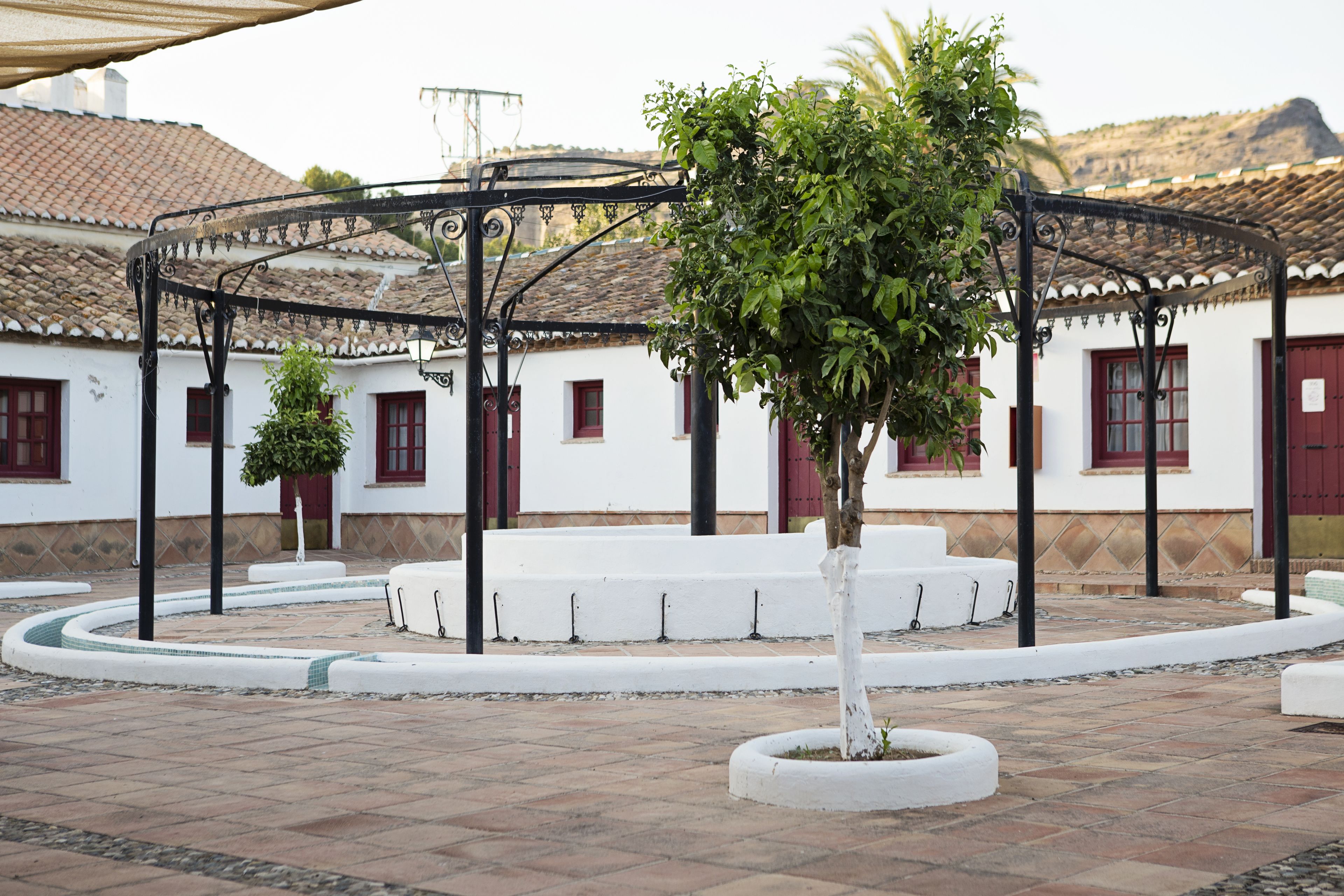 Une cour intérieure agrémentée d’une pergola, de bancs blancs et d’un arbre au centre.