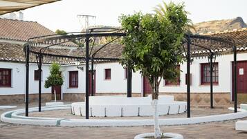 A courtyard with a pergola, white benches, and a tree in the center.