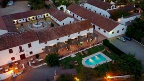 Vue aérienne d’une cour avec une piscine, entourée de bâtiments blancs aux toits recouverts de tuiles rouges.