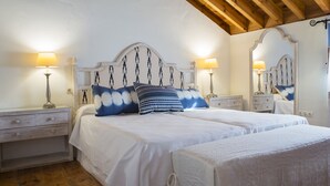 Une chambre avec un plafond en bois, un lit avec une literie blanche et des oreillers bleus, deux tables de chevet avec des lampes et un miroir sur le mur.