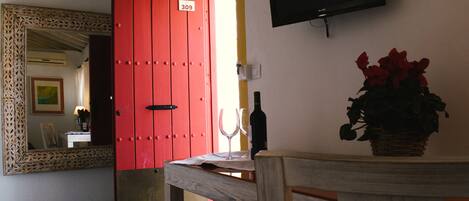 A room with a red door, a wooden table, a bottle, and a vase of flowers.