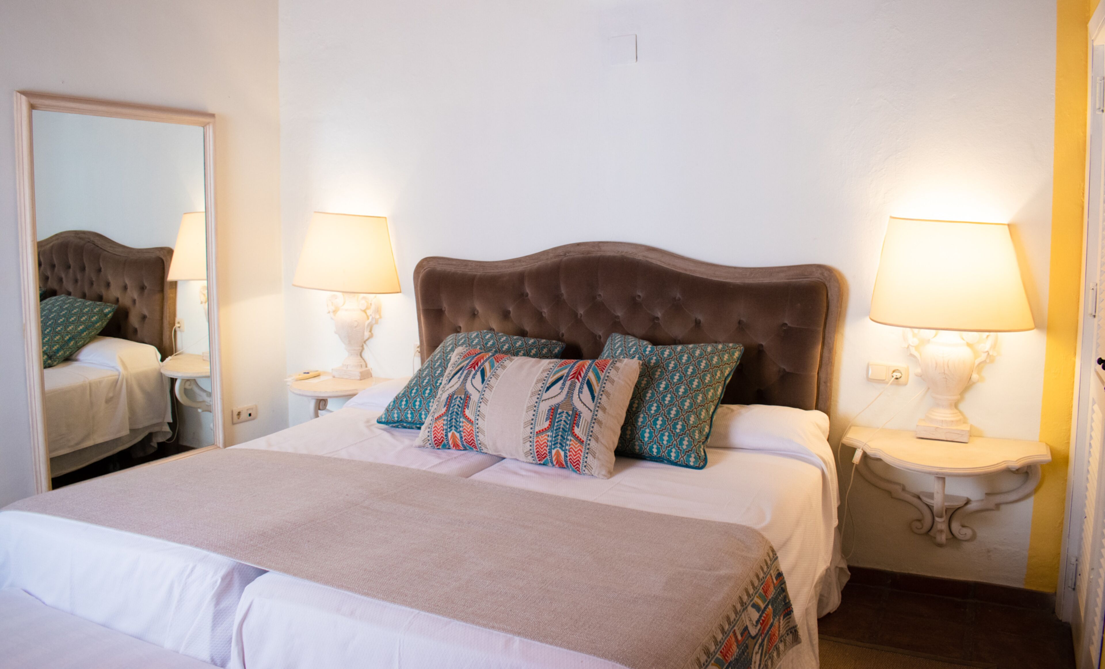 A neatly made bed with patterned pillows, a tufted headboard, and bedside lamps on white nightstands.