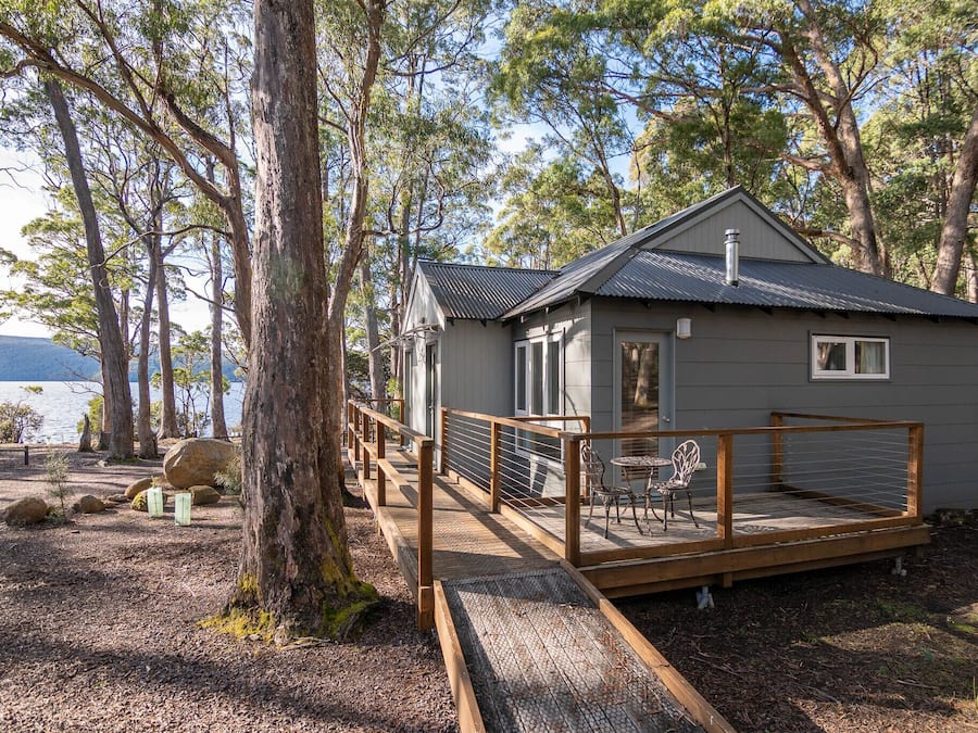A cabin with a deck, surrounded by trees and a lake.