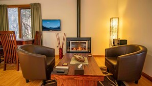 Una sala de estar acogedora con chimenea, sillones de cuero, una mesa de centro de madera y un televisor en la pared.