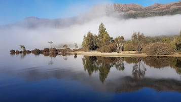 A calm lake with clear reflections, surrounded by trees and a mountain in the background.