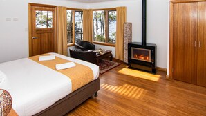 Habitación de hotel con cama, una silla, un escritorio, chimenea y ventanas grandes con cortinas.