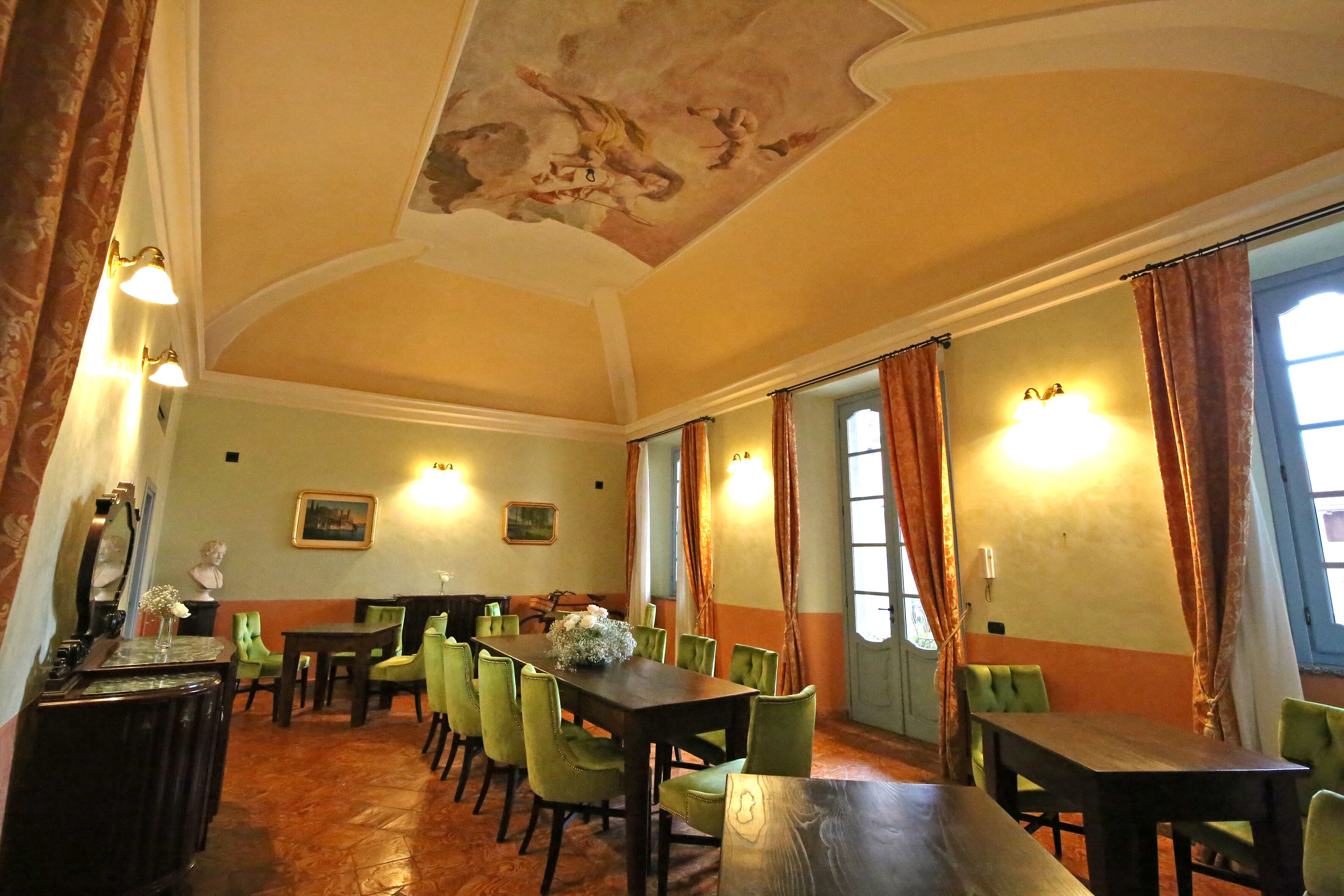 A dining area with a long table, green chairs, and a ceiling mural.