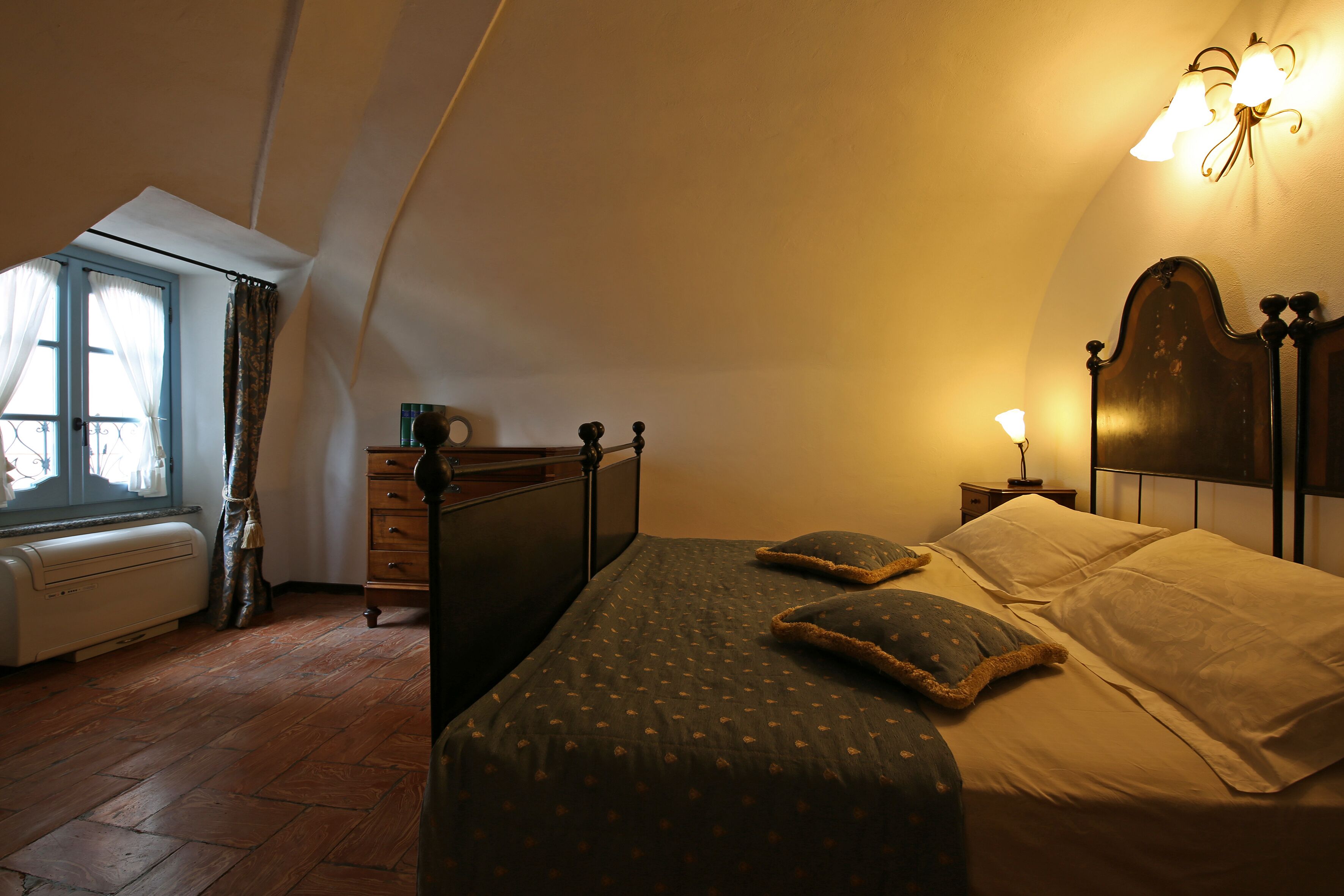 A bedroom with a bed, a dresser, a nightstand, and a window with curtains.