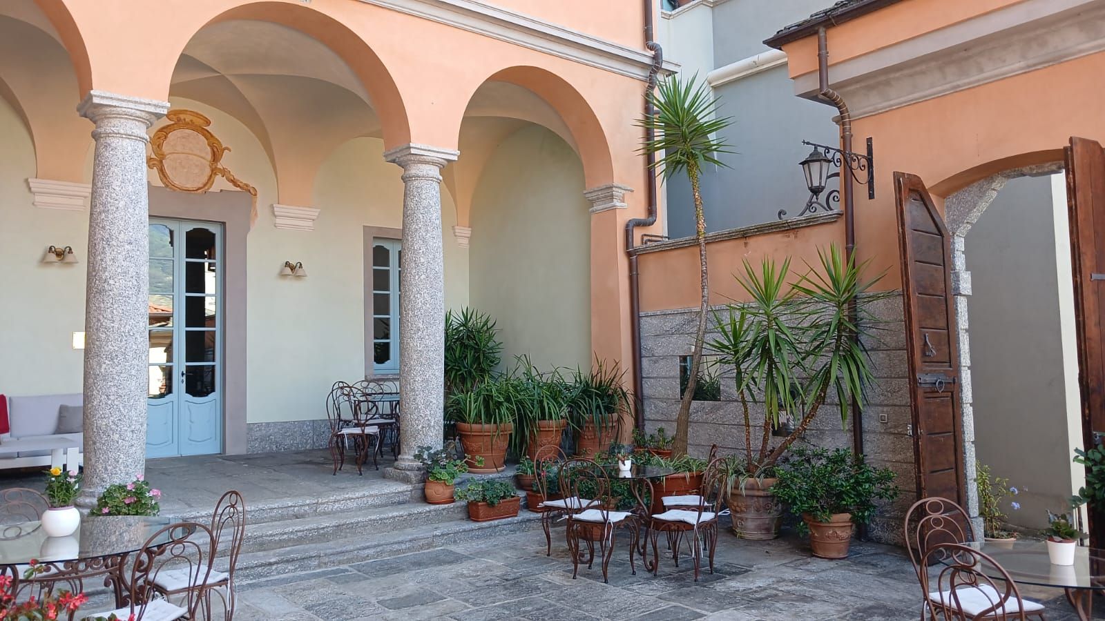 An outdoor patio with stone columns, tables, chairs, and potted plants.