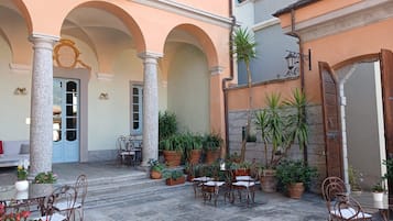 An outdoor patio with stone columns, tables, chairs, and potted plants.