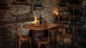 A stone-walled room with a round wooden table, candles, and wine bottles. - Palazzo del Vicerè  (Lezzeno)