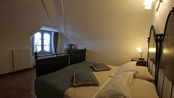 Une chambre avec deux lits, une fenêtre avec des rideaux, un radiateur et une table de chevet avec une lampe.