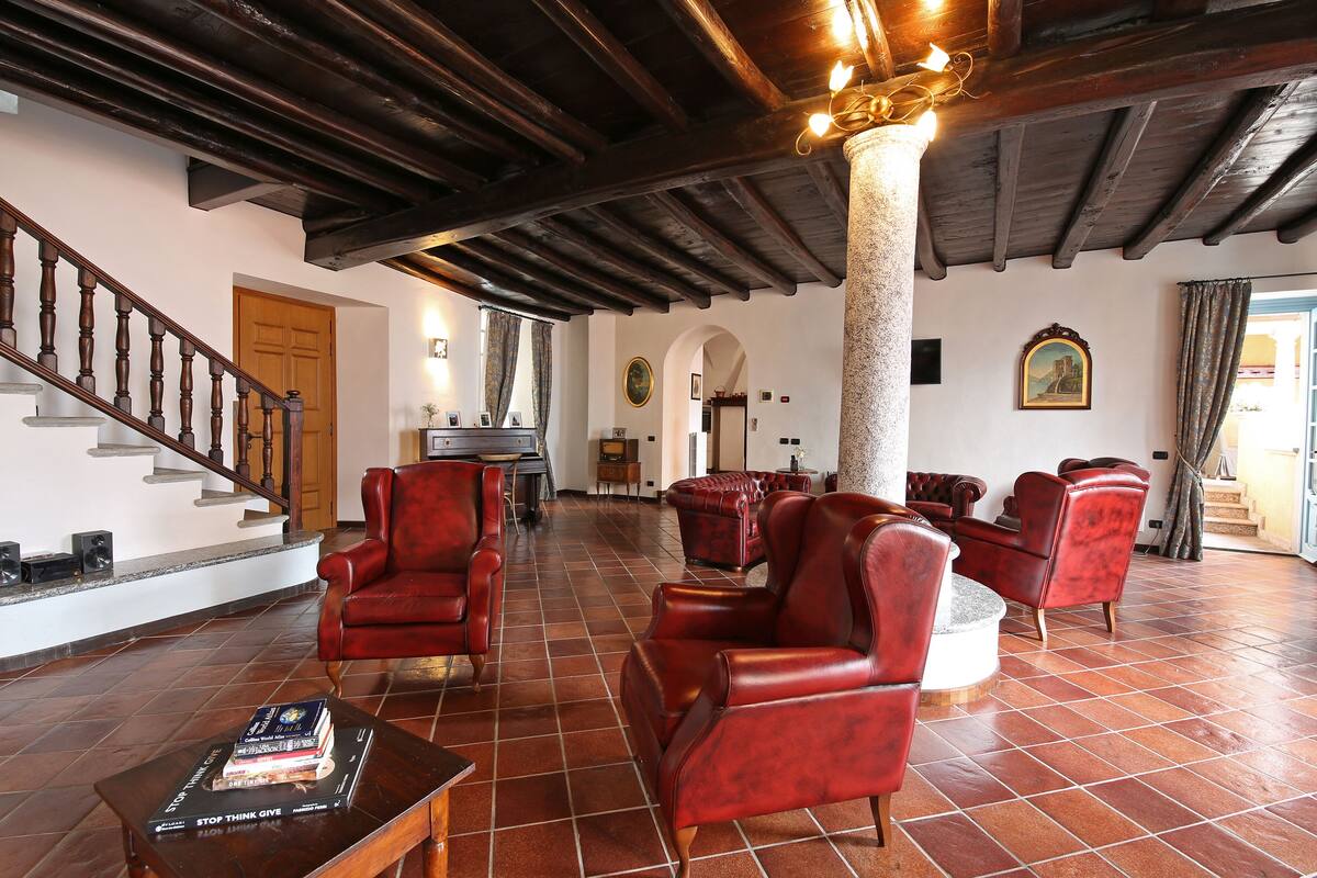 A spacious living area with a high ceiling, red leather armchairs, a fireplace, and a staircase leading to another level.