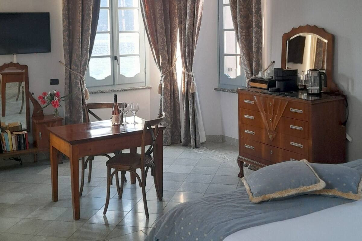 A hotel room with a bed, a wooden dresser, a desk with chairs, a television, and a window with curtains.
