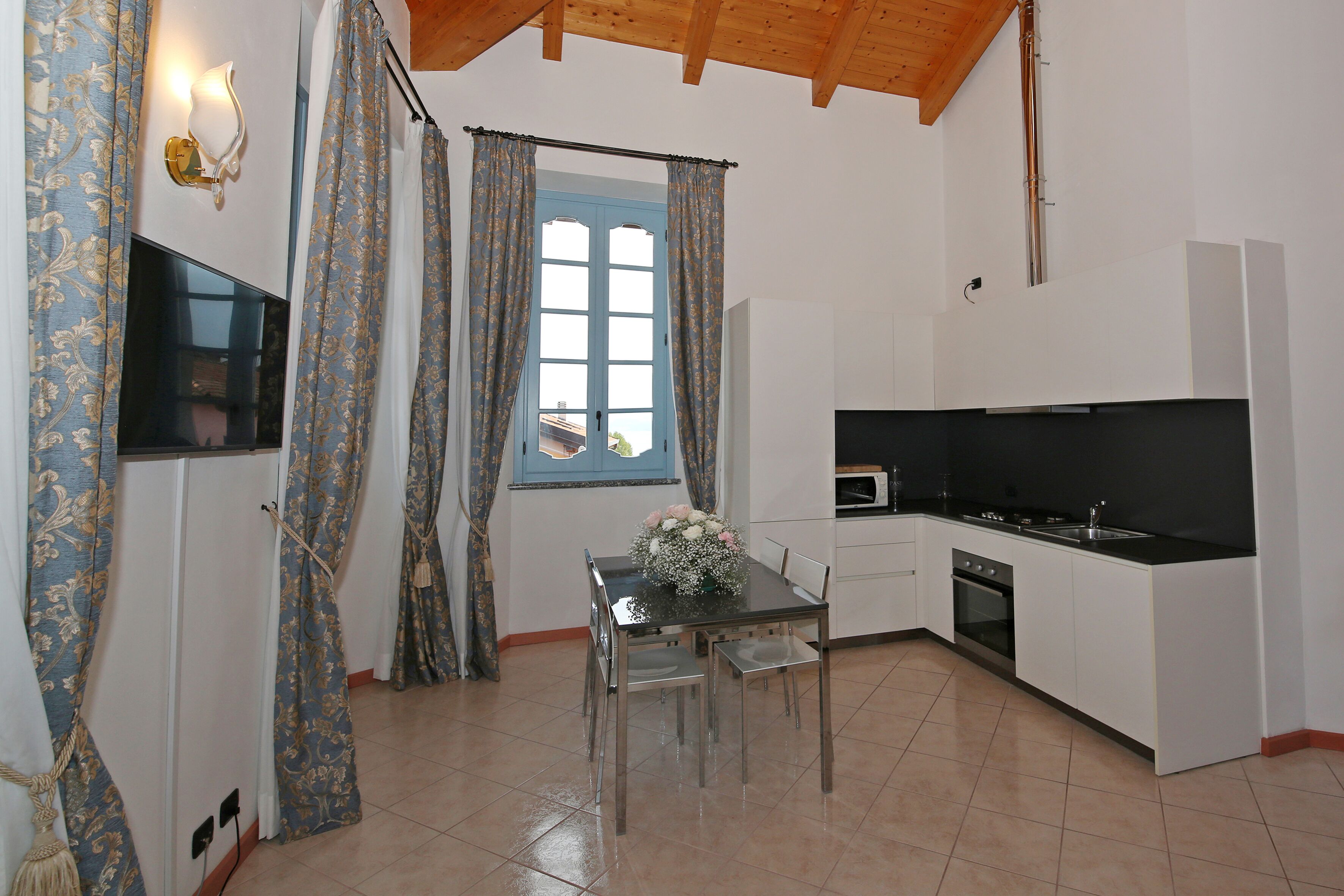 A compact kitchen with white cabinets, a black countertop, and a window with blue curtains.