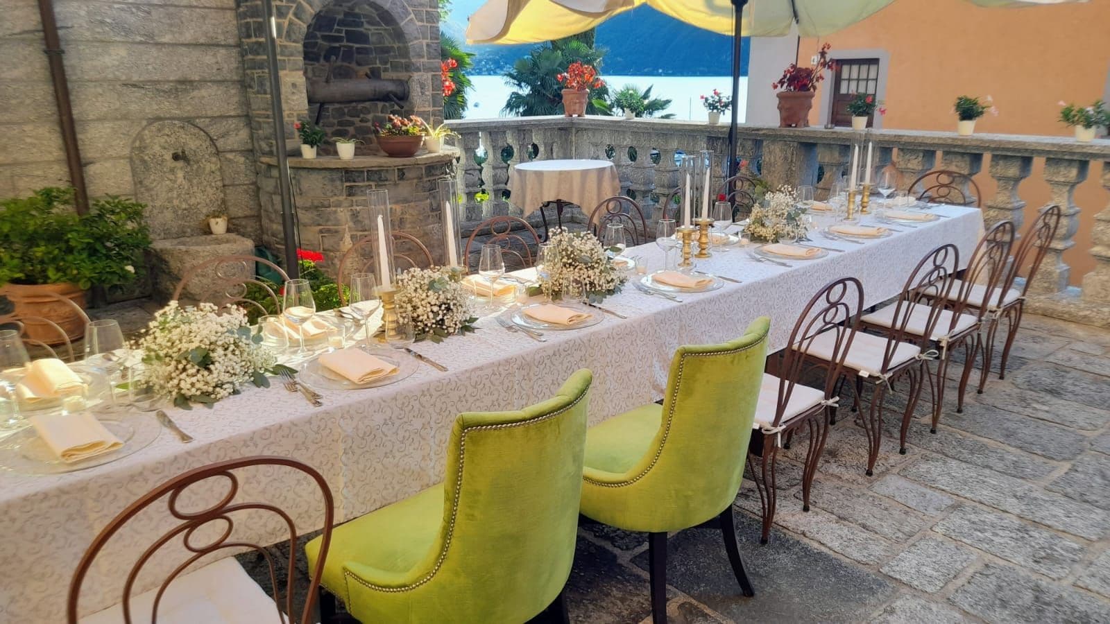 An outdoor dining area with a stone wall, a table set for a meal, and chairs.