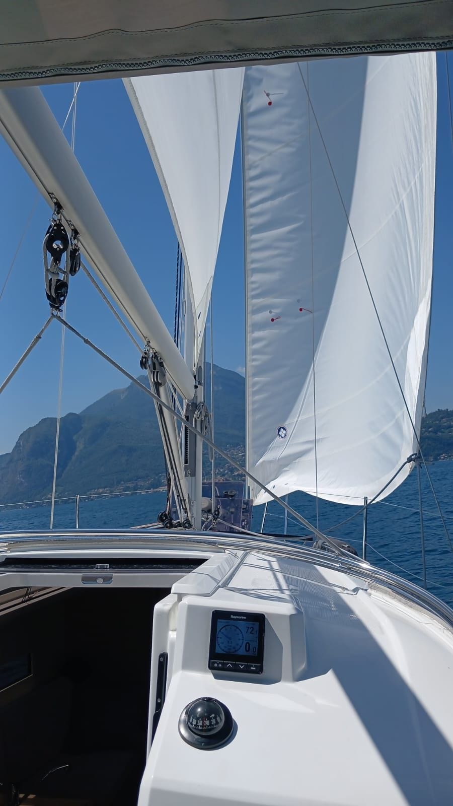 A sailboat with white sails, a digital display, and a mountainous coastline in the background.