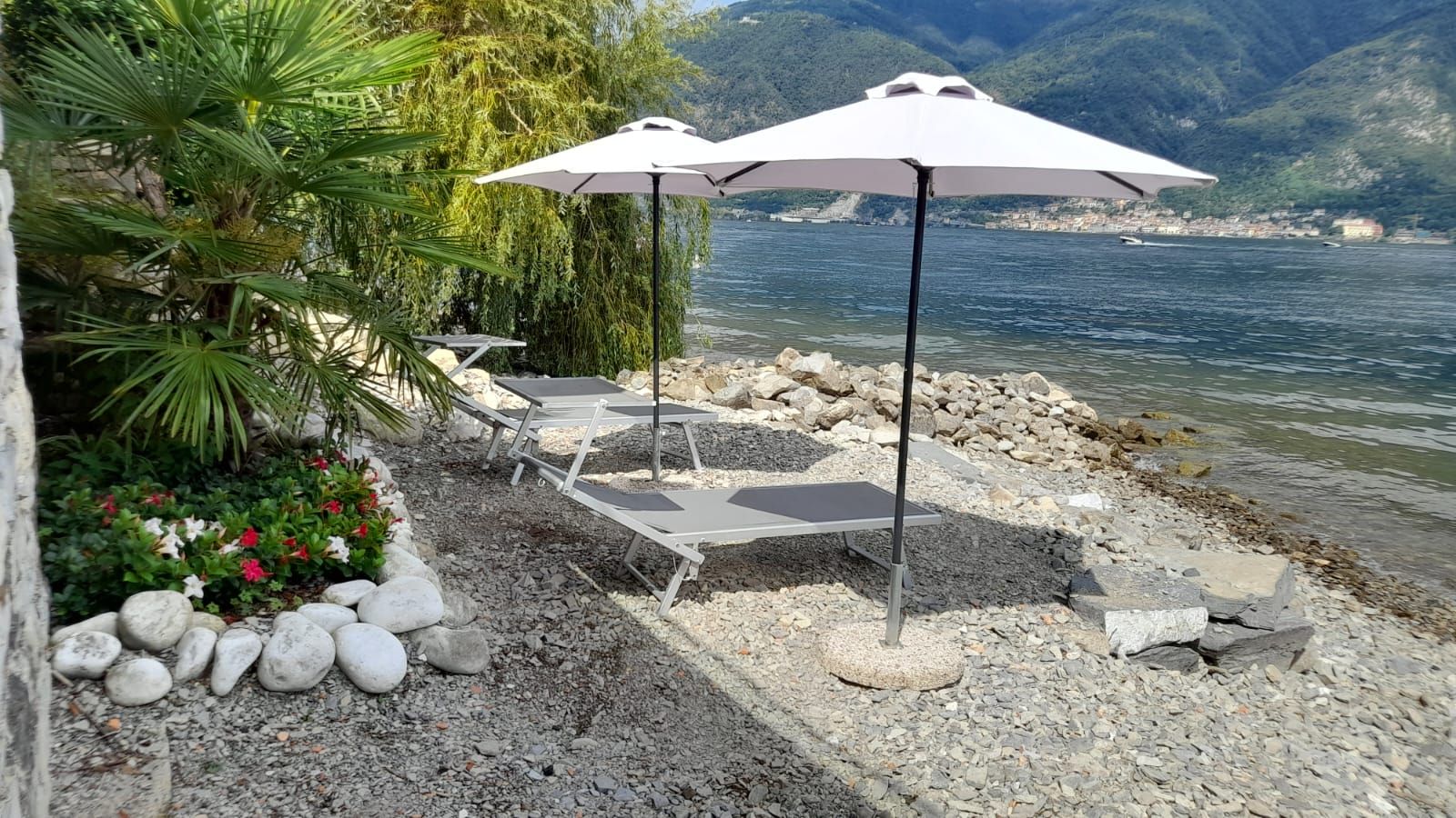 Ein Sitzbereich am Seeufer mit zwei weißen Sonnenschirmen, einem Tisch und Stühlen.