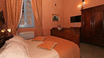 Ein Schlafzimmer mit einem Bett, Vorhängen, einem Nachttisch, einer Lampe, einem an der Wand montierten Fernseher und einem Holzschrank.
