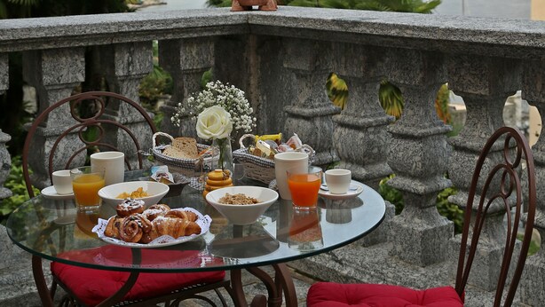 A table with breakfast items, a glass of orange juice, and a view of a lake and mountains. - Palazzo del Vicerè  (Lezzeno)