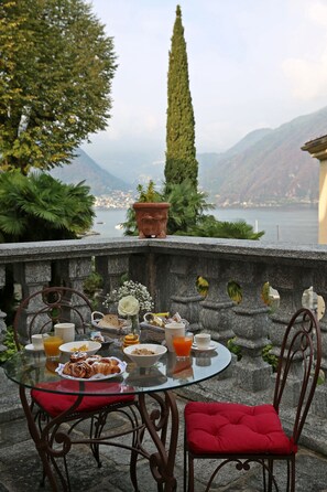 A table with breakfast items, a glass of orange juice, and a view of a lake and mountains. - Palazzo del Vicerè  (Lezzeno)