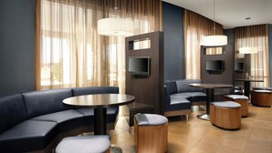 A modern hotel lobby with a curved sofa, round tables, and ottomans. - Courtyard Hammond (Hammond)