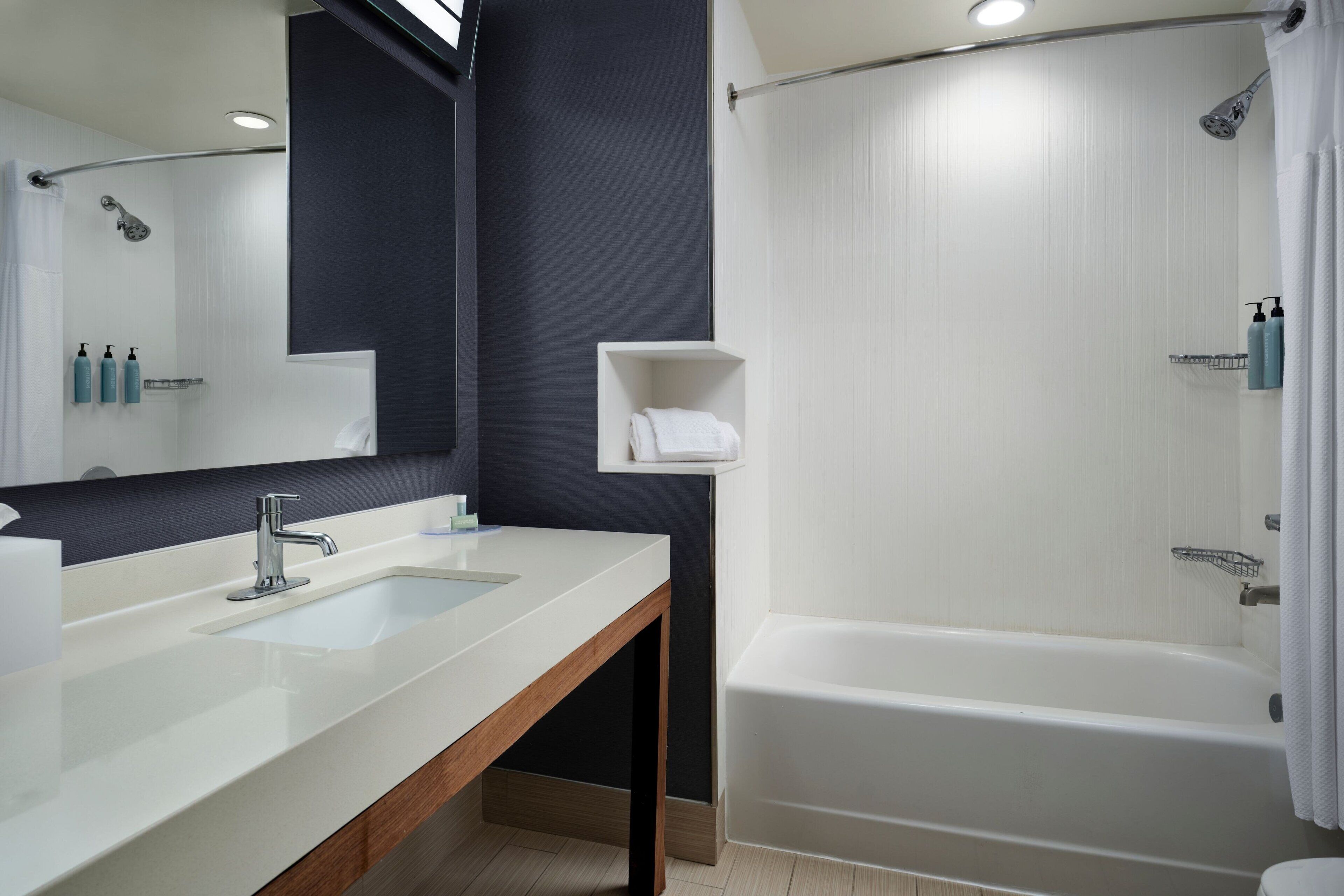 A modern bathroom with a double sink, a large mirror, a bathtub, and a towel rack.