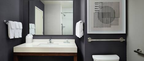 A modern bathroom with a white sink, dark walls, a large mirror, a framed artwork, and a white toilet.