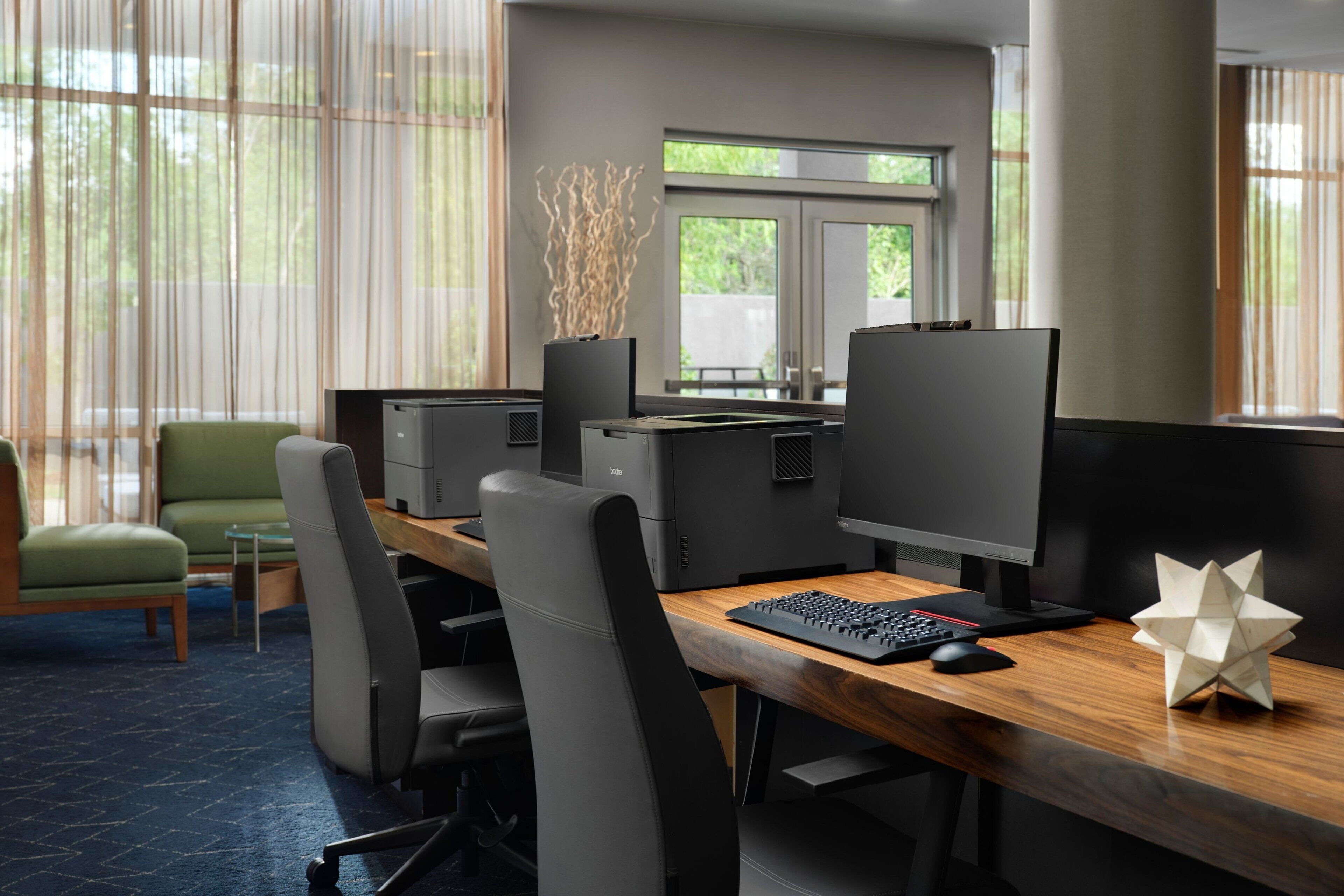 Ein moderner Arbeitsplatz mit mehreren Arbeitsstationen, ergonomischen Stühlen und einem großen Fenster, das für natürliches Licht sorgt.