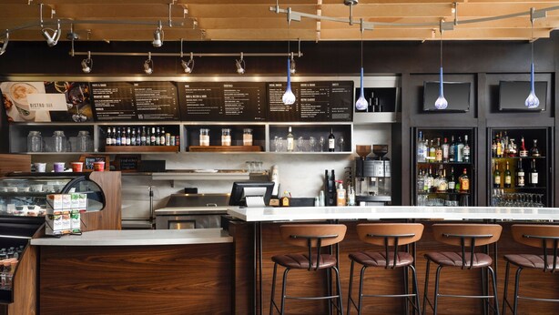 A bar area with a wooden counter, bar stools, and a menu board. - Courtyard Hammond (Hammond)