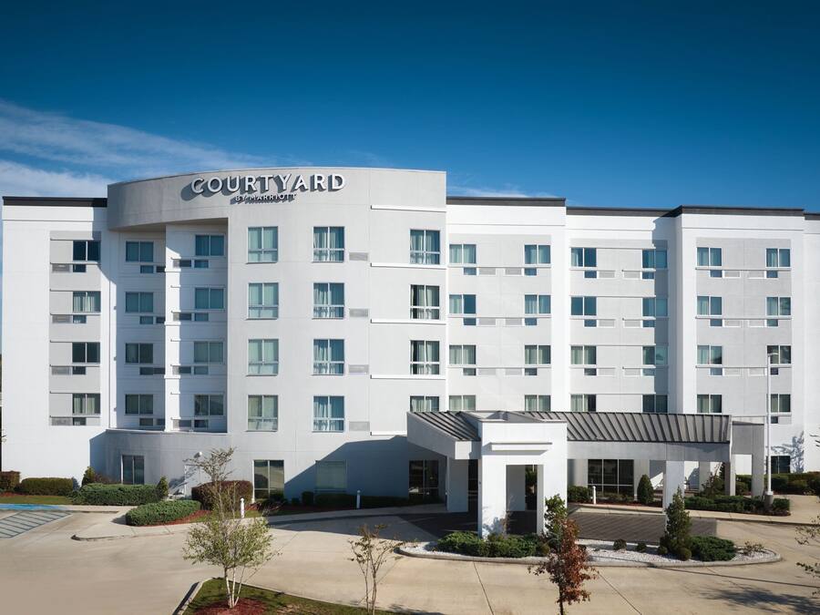 Ein Hotel der Courtyard by Marriott-Kette mit modernem Design, das einen zentralen Eingang, mehrere Stockwerke und einen Parkbereich zeigt.