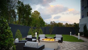 An outdoor patio area with wicker furniture, a central fire pit, and a paved floor. - Courtyard Hammond (Hammond)