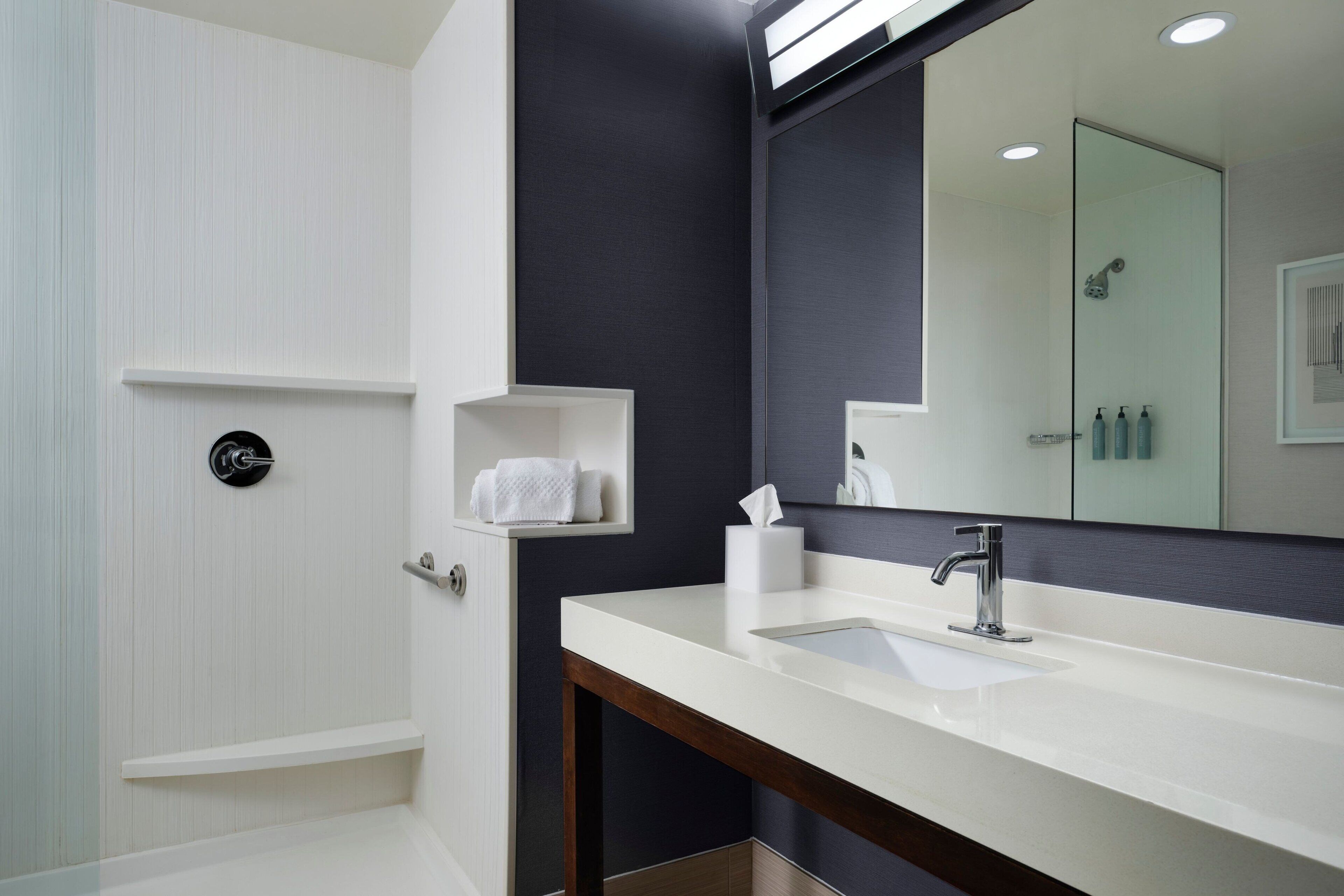 A modern bathroom with a large mirror, a white sink, and a shower area.