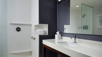 A modern bathroom with a large mirror, a white sink, and a shower area.