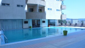 A swimming pool with a tiled deck, surrounded by a building with balconies and windows.