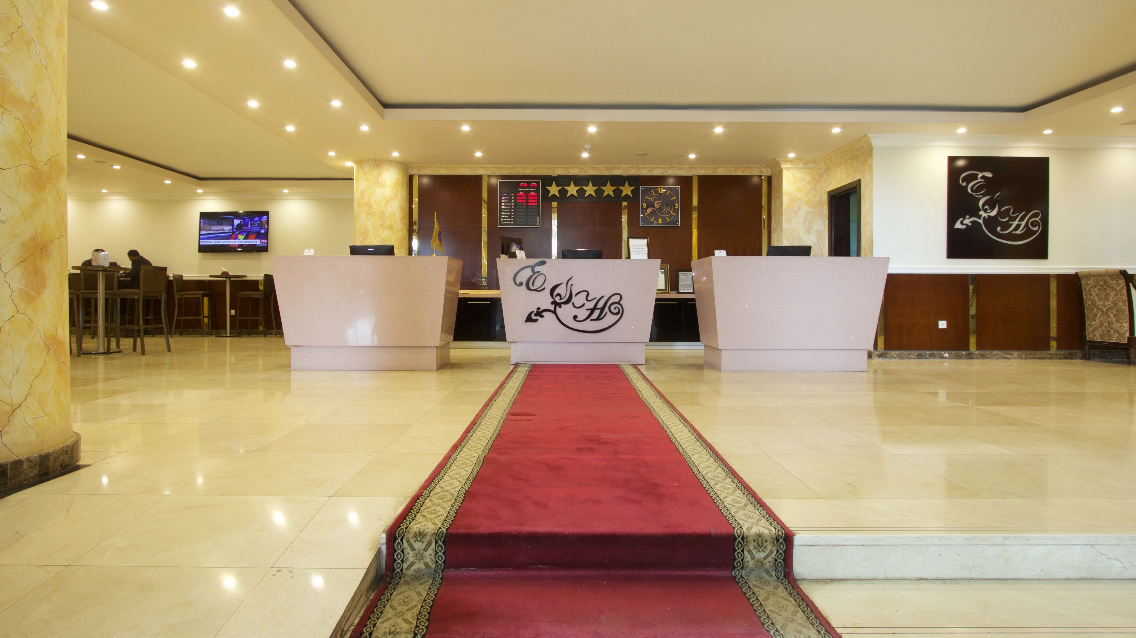 A hotel lobby with a reception desk, a red carpet, and a television screen in the background.