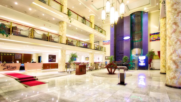A multi-level hotel lobby with a reception desk, seating areas, and a red carpeted staircase.