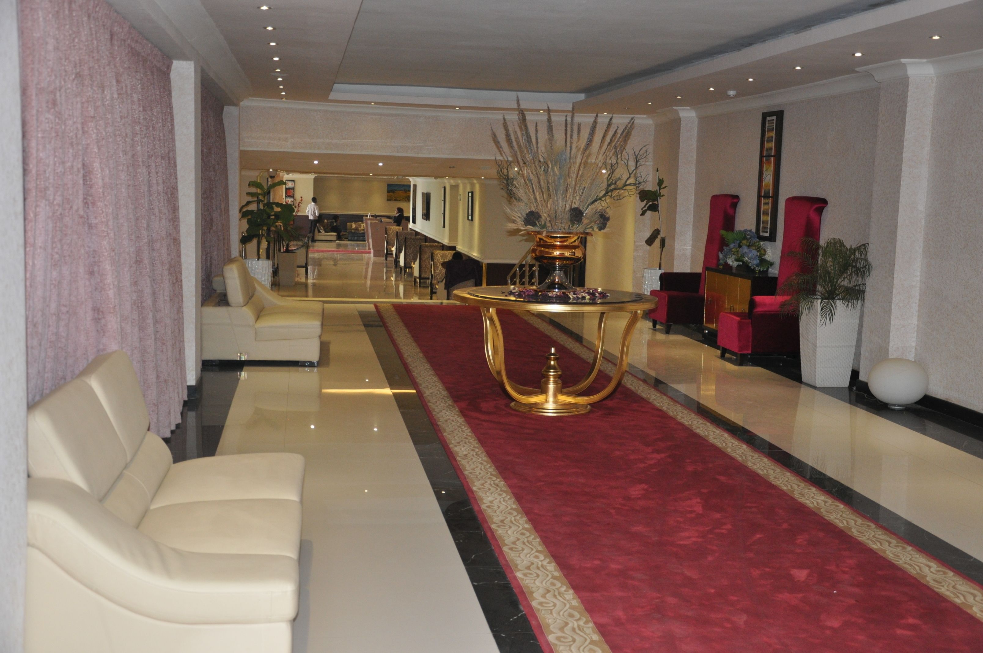 A spacious lobby with a red carpet, a gold table centerpiece, and a white sofa.