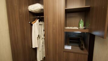 A wooden wardrobe with a hanging robe and a shelf with a green iron and a small item on it.