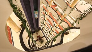 A multi-level atrium with a central staircase, surrounded by plants and decorative railings.