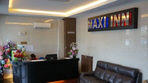 A hotel reception area with a black reception desk, a brown leather sofa, and a large 'MAXI INN' sign.