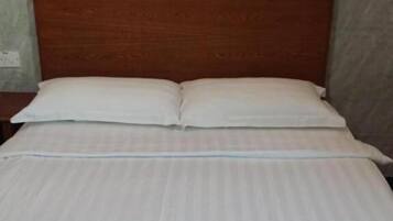 A neatly made bed with a wooden headboard, white linens, and a plain wall with a subtle pattern.