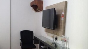 A small room with a black chair, a TV mounted on the wall, a wooden shelf, and a glass table with a red cloth.